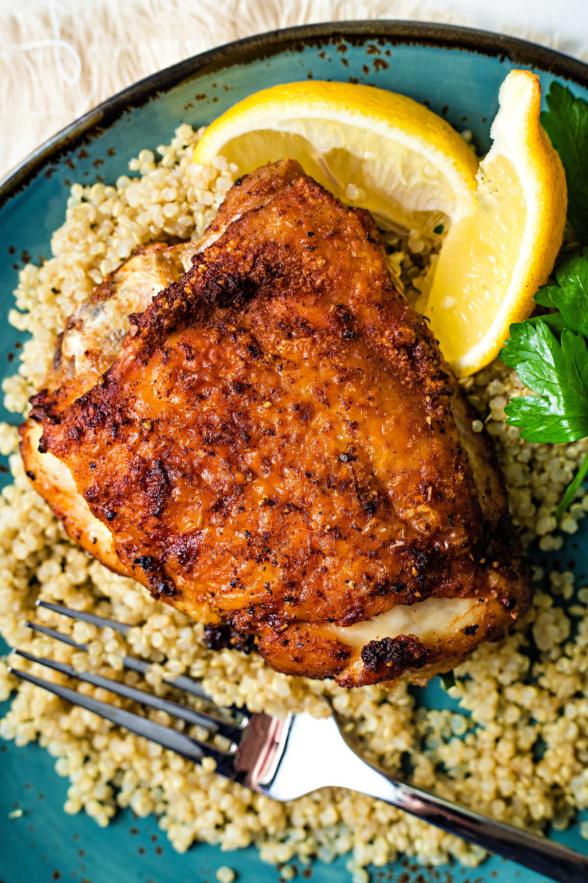 an air fryer chicken thigh on a bed of couscous on a blue plate with a lemon wedge garnish.
