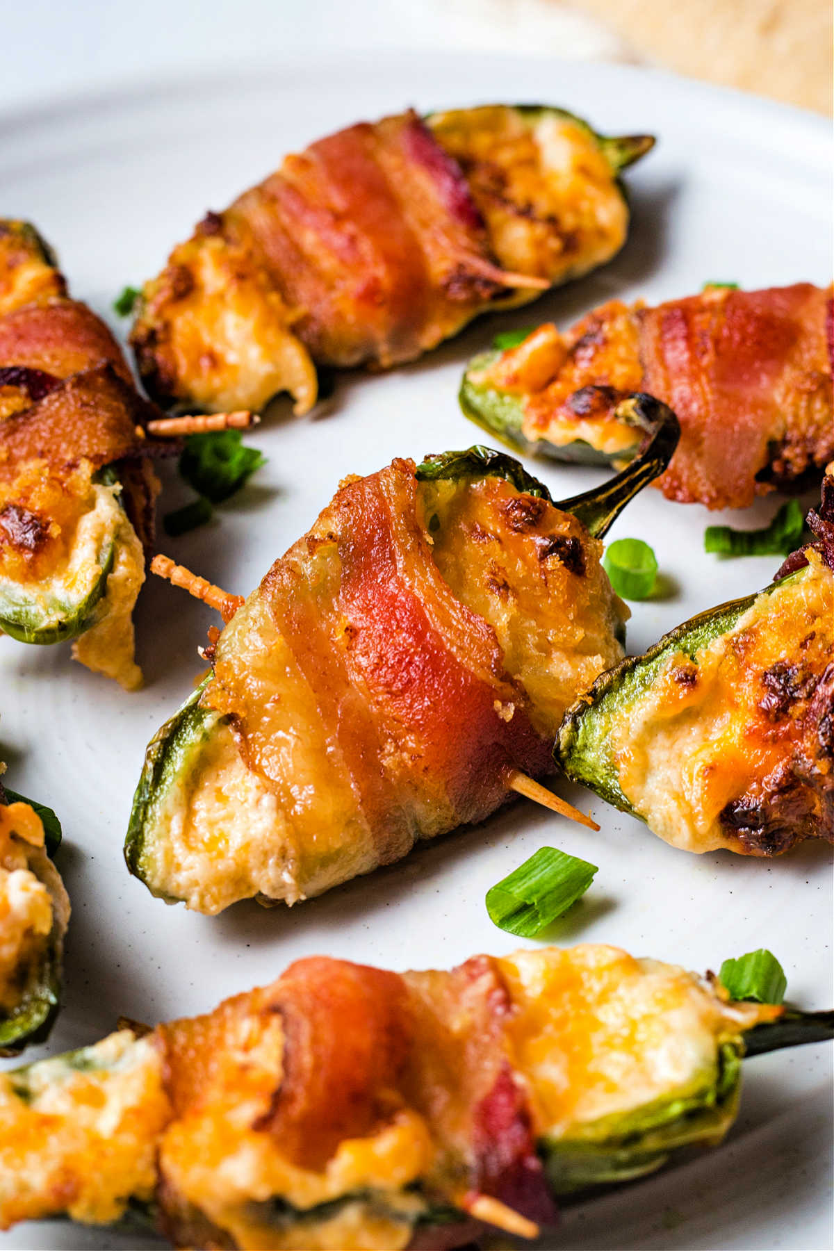 bacon wrapped jalapeno poppers on a white plate garnished with sliced green onion tops.