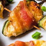 bacon wrapped jalapeno poppers on a white plate garnished with sliced green onion tops.