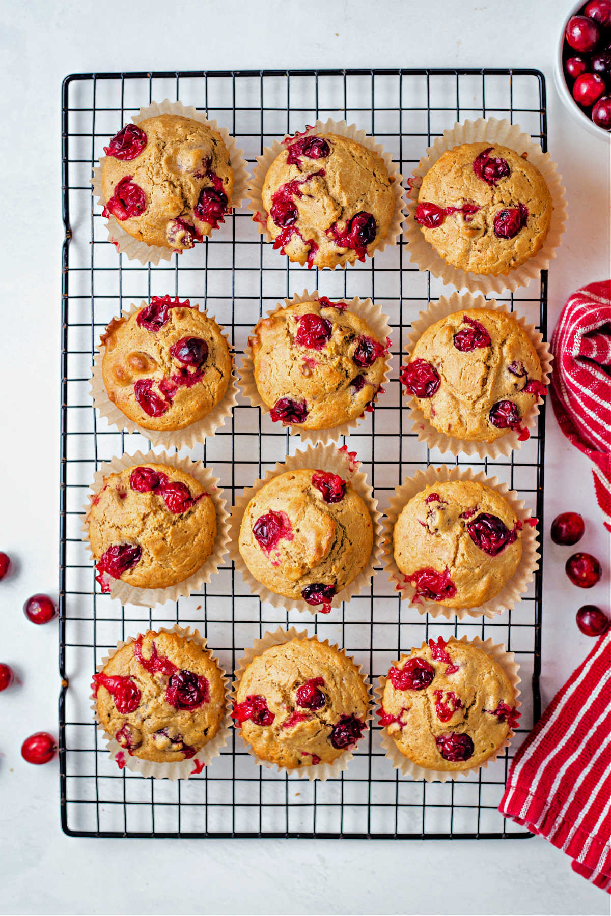 a dozen orange cranberry muffins on a cooling rack with cranberries scattered around.