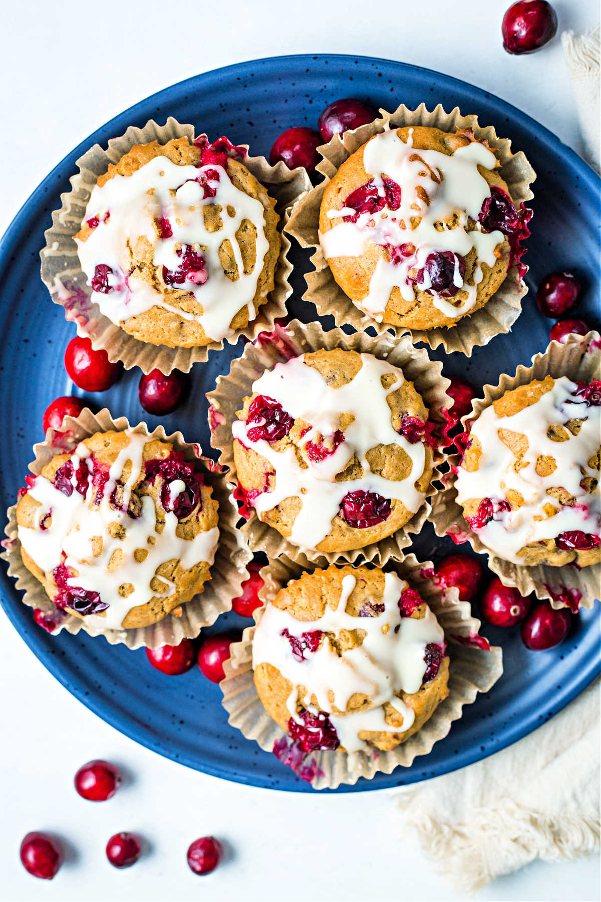 orange cranberry muffins on a blue plate with cranberries scattered on a table.