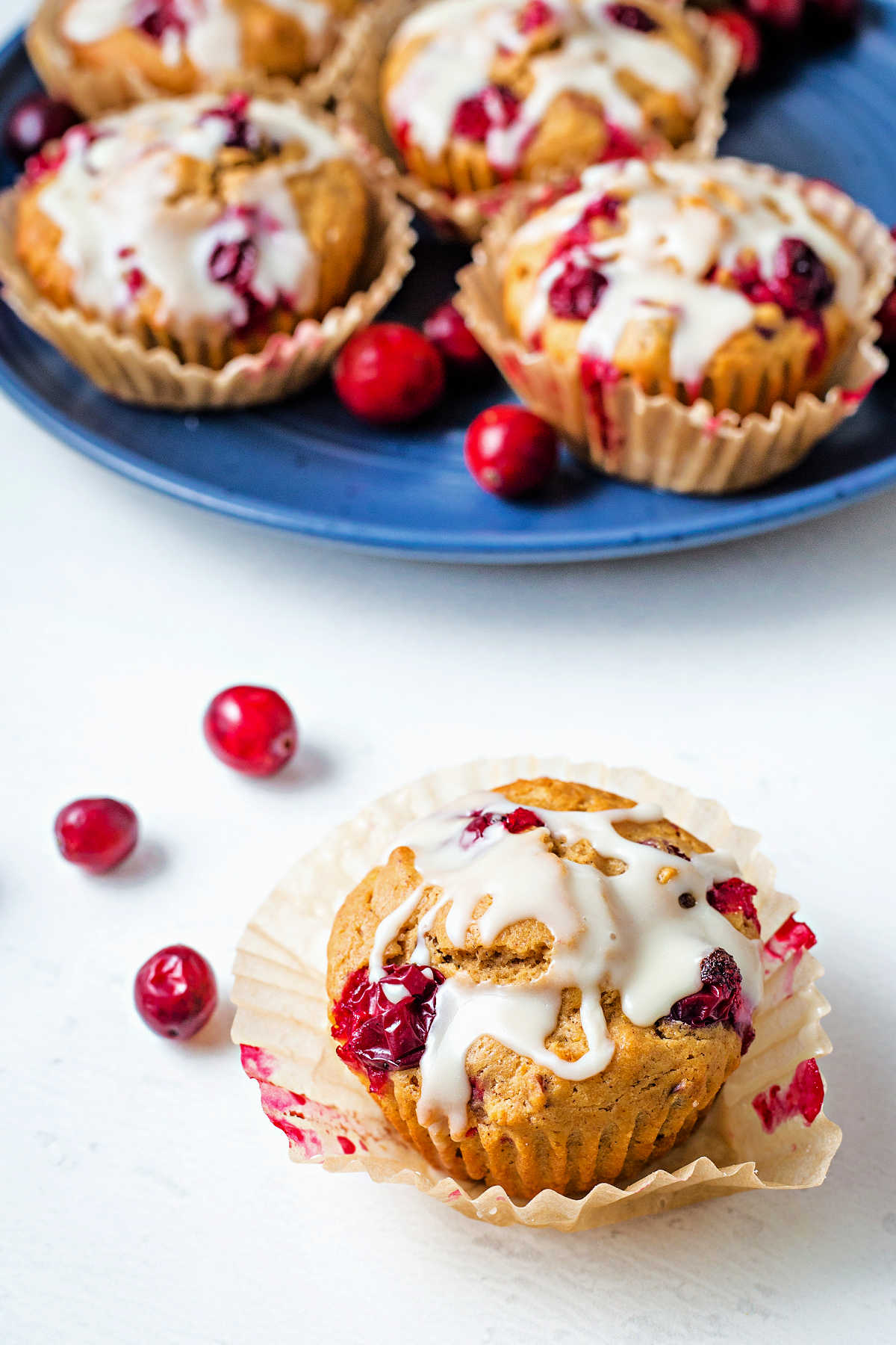 an orange cranberry muffin in a parchment paper liner on a table with a plate of muffins in the background.