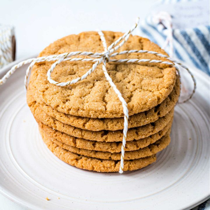 a stack of chewy peanut butter cookies tied together with a string sitting on a white plate with a blue striped napkin nestled by the plate.