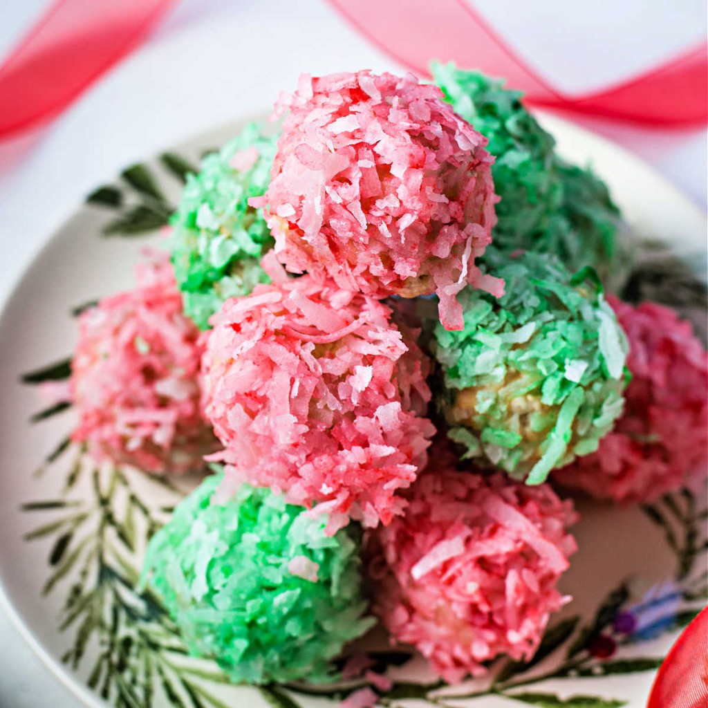 red and green coconut balls stacked on a holiday plate.
