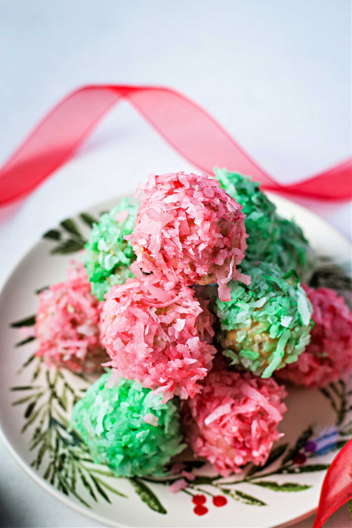 red and green coconut balls stacked on a holiday plate.