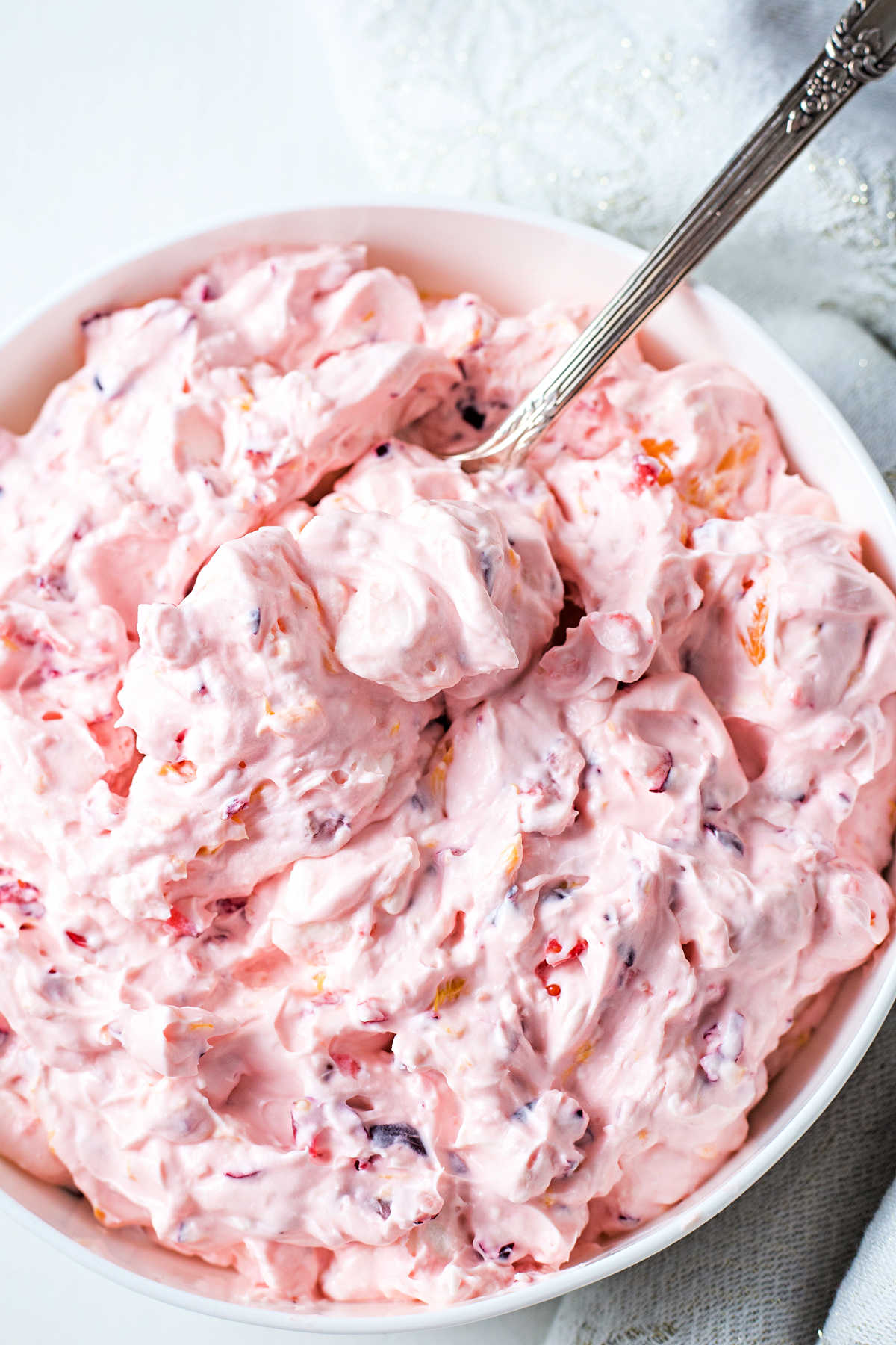 a serving spoon nestled into a bowl of cranberry fluff sitting on a table.