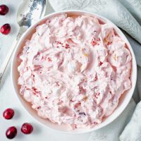 a bowl of creamy cranberry fluff sitting on a table with cranberries scattered around.