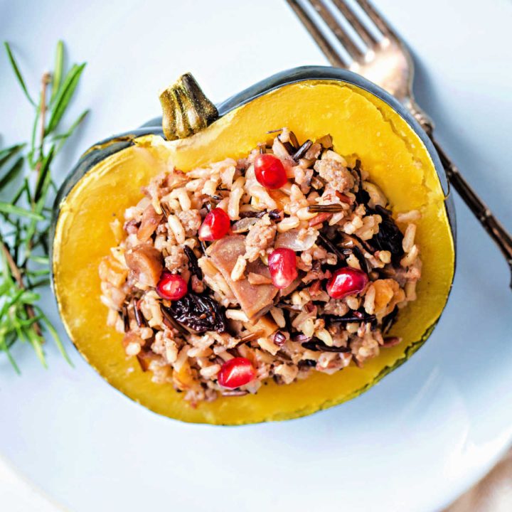 instant pot acorn squash stuffed with wild rice and sausage on a white plate with a sprig or rosemary and a fork.