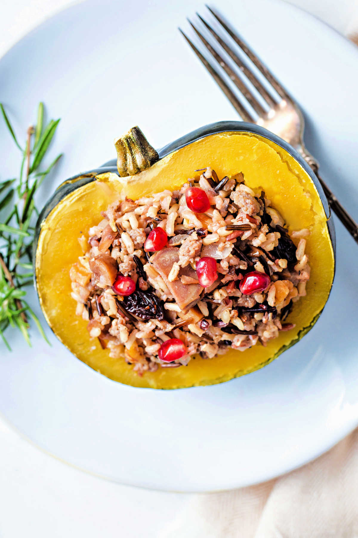 instant pot acorn squash stuffed with wild rice and sausage on a white plate with a sprig or rosemary and a fork.