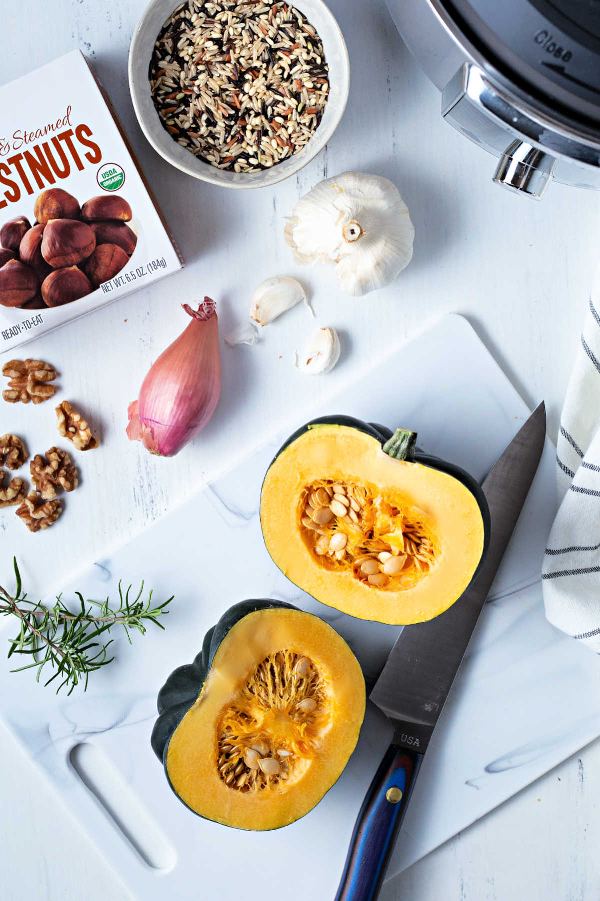 a few ingredients for making instant pot stuffed acorn squash on a table, including squash, shallot, garlic, wild rice and steamed chestnuts.
