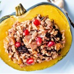 instant pot acorn squash stuffed with wild rice and sausage on a white plate with a sprig or rosemary and a fork.