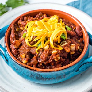 a bowl of slow cooker southwest chili garnished with shredded cheese sitting on a plate.