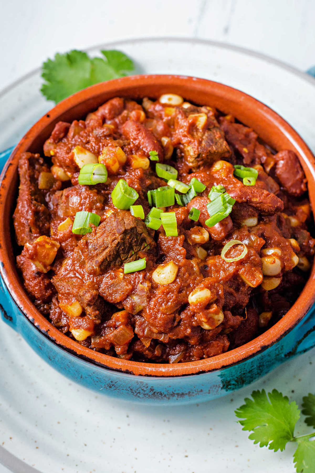 a bowl of slow cooker southwest chili garnished with green onions and cilantro on a plate.