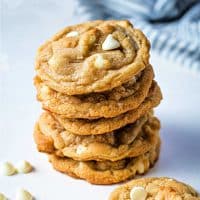 white chocolate macadamia nut cookies stacked on top of each other to make a tower with white chocolate chips scattered around.