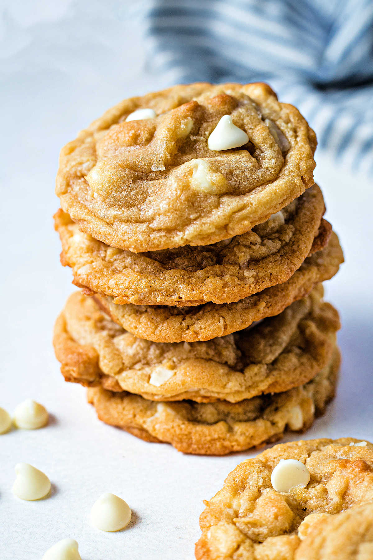 white chocolate macadamia nut cookies stacked on top of each other to make a tower with white chocolate chips scattered around.