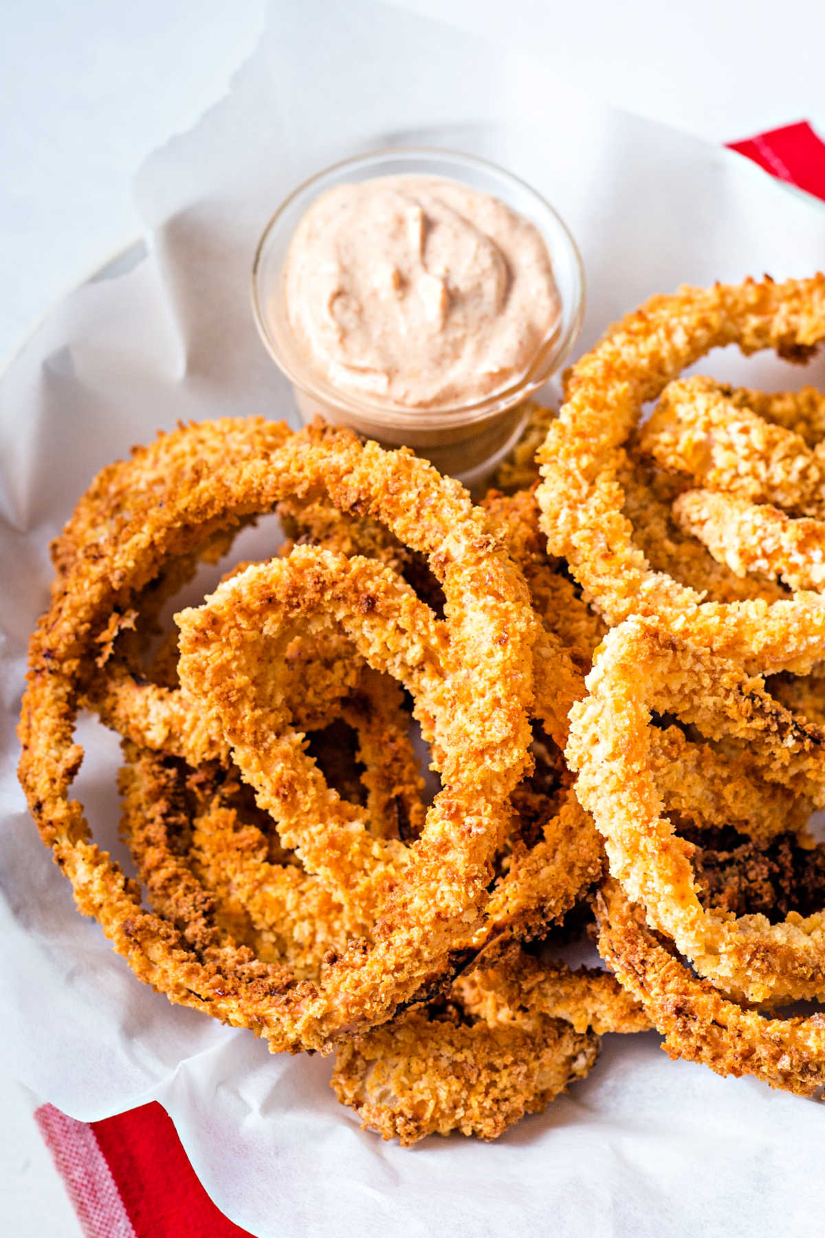 air fried onion rings in a bowl lined with parchment paper with a cup of dipping sauce.