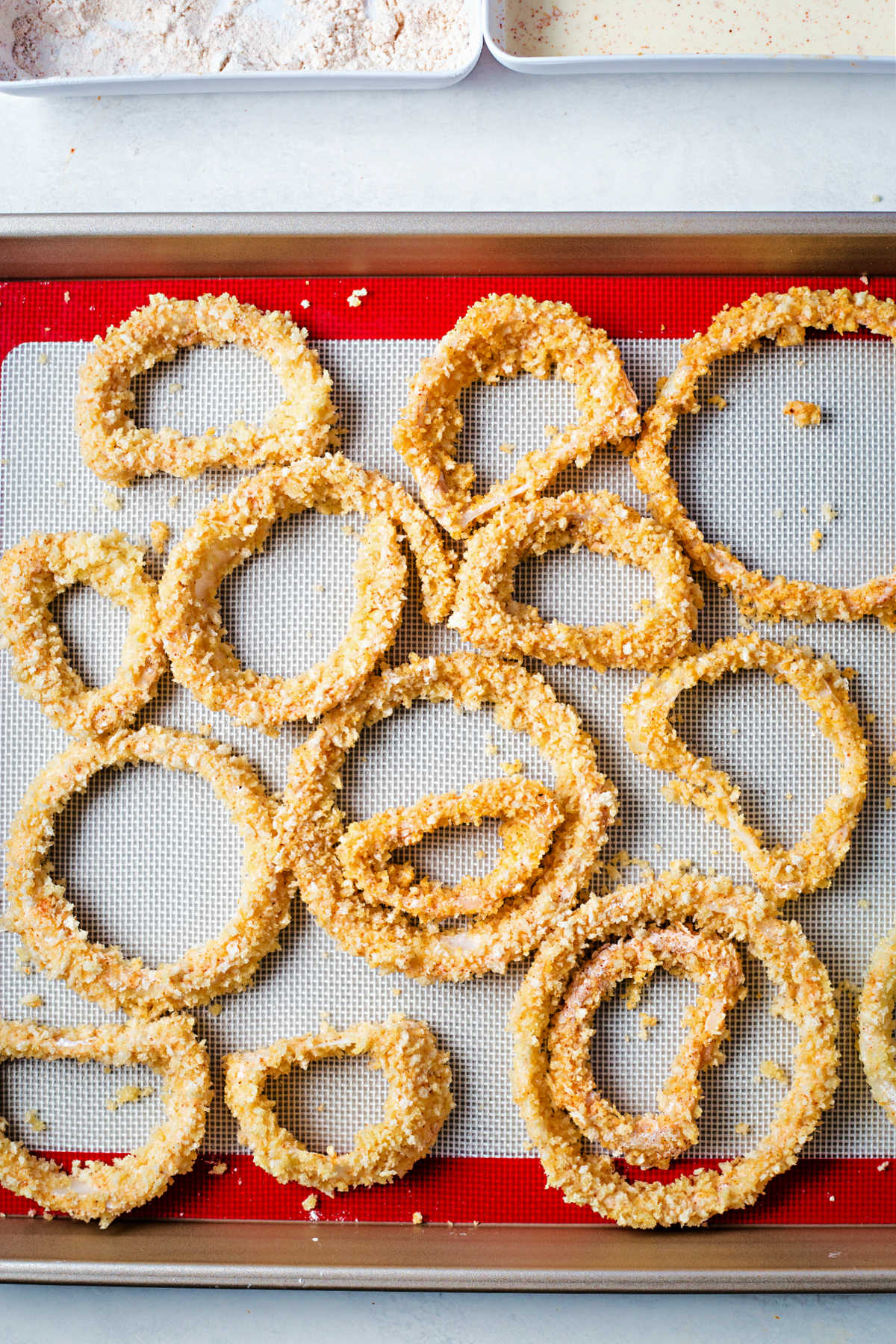 breaded onion rings on a silicone mat on a baking sheet.