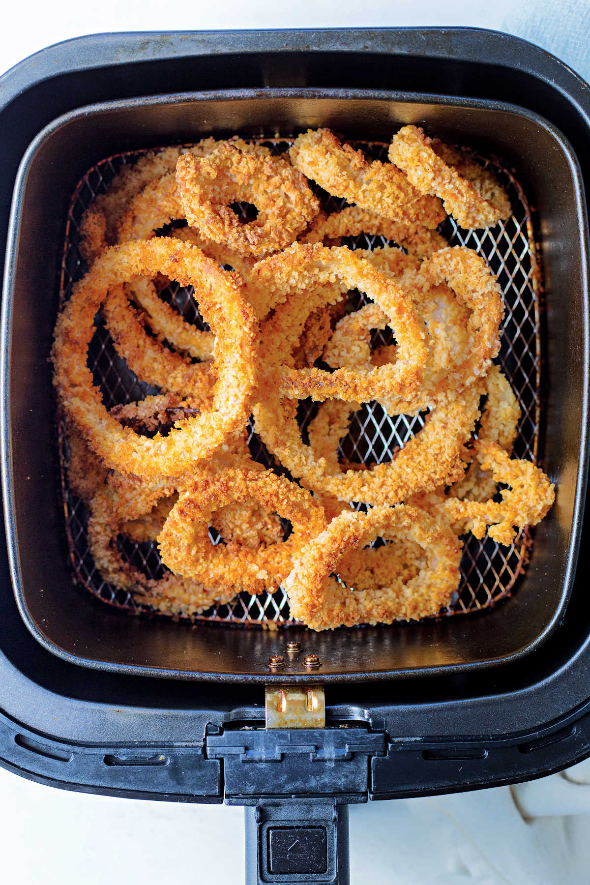 warming up air fried onion rings stacked in the basket of an air fryer.