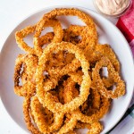 a bowl of air fried onion rings with a dish of dipping sauce to the side.