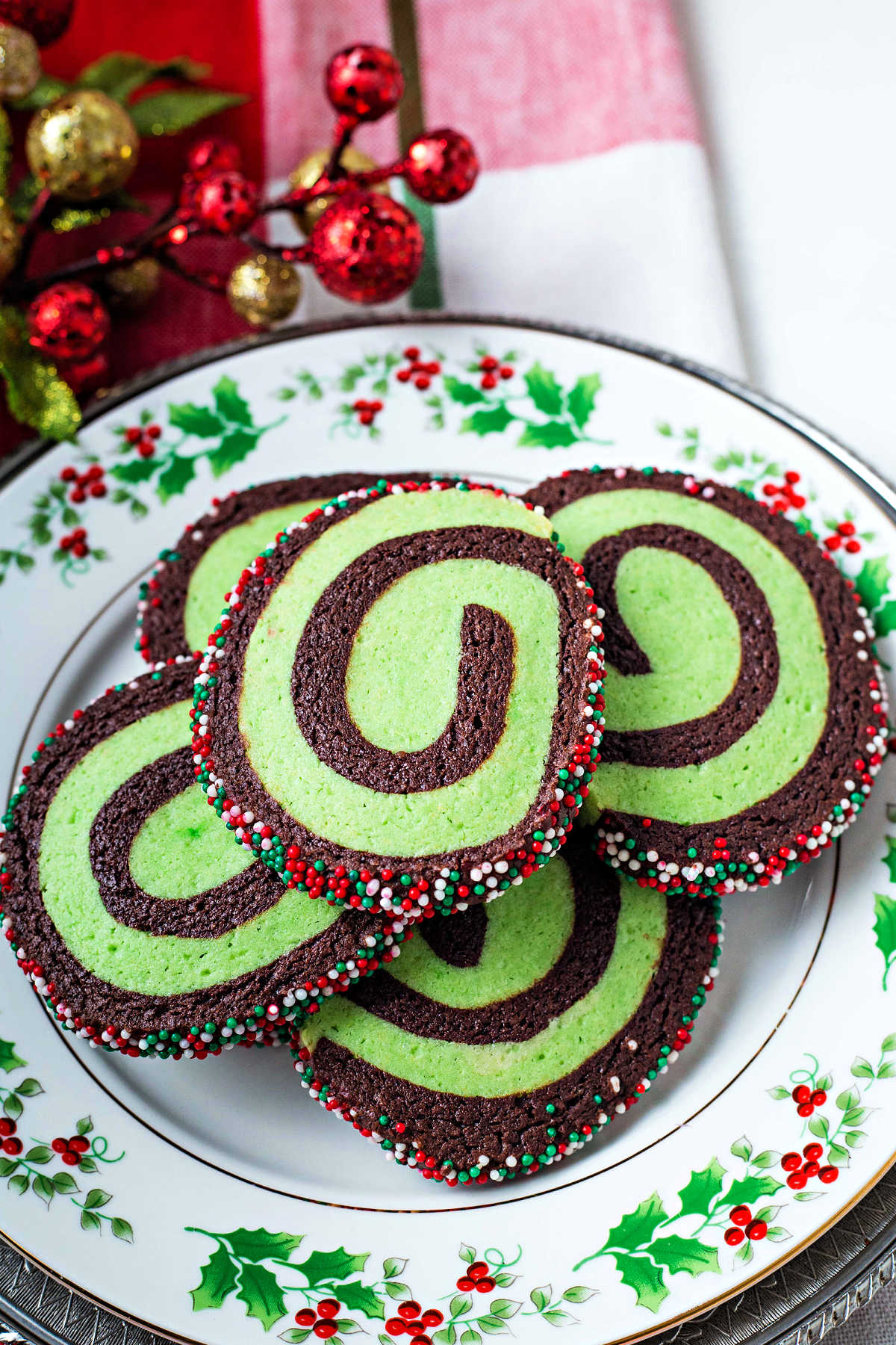 chocolate mint pinwheel cookies stacked on a Christmas plate setting on a table.
