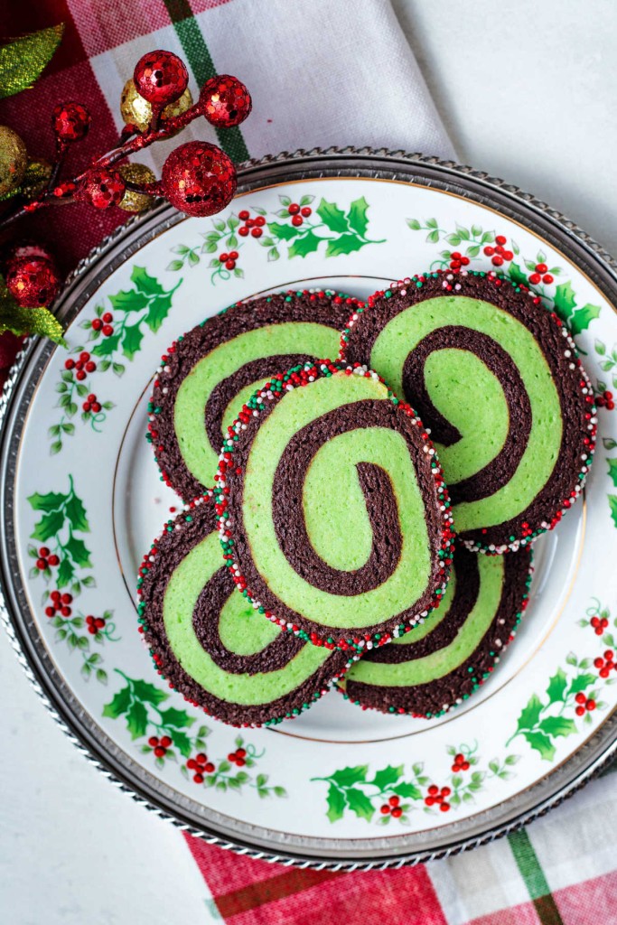 chocolate mint pinwheel cookies stacked on a Christmas plate setting on a table.