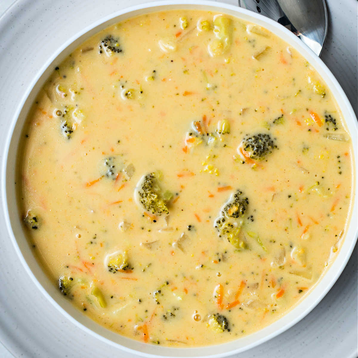 a close up shot of a bowl of crockpot broccoli cheddar soup.