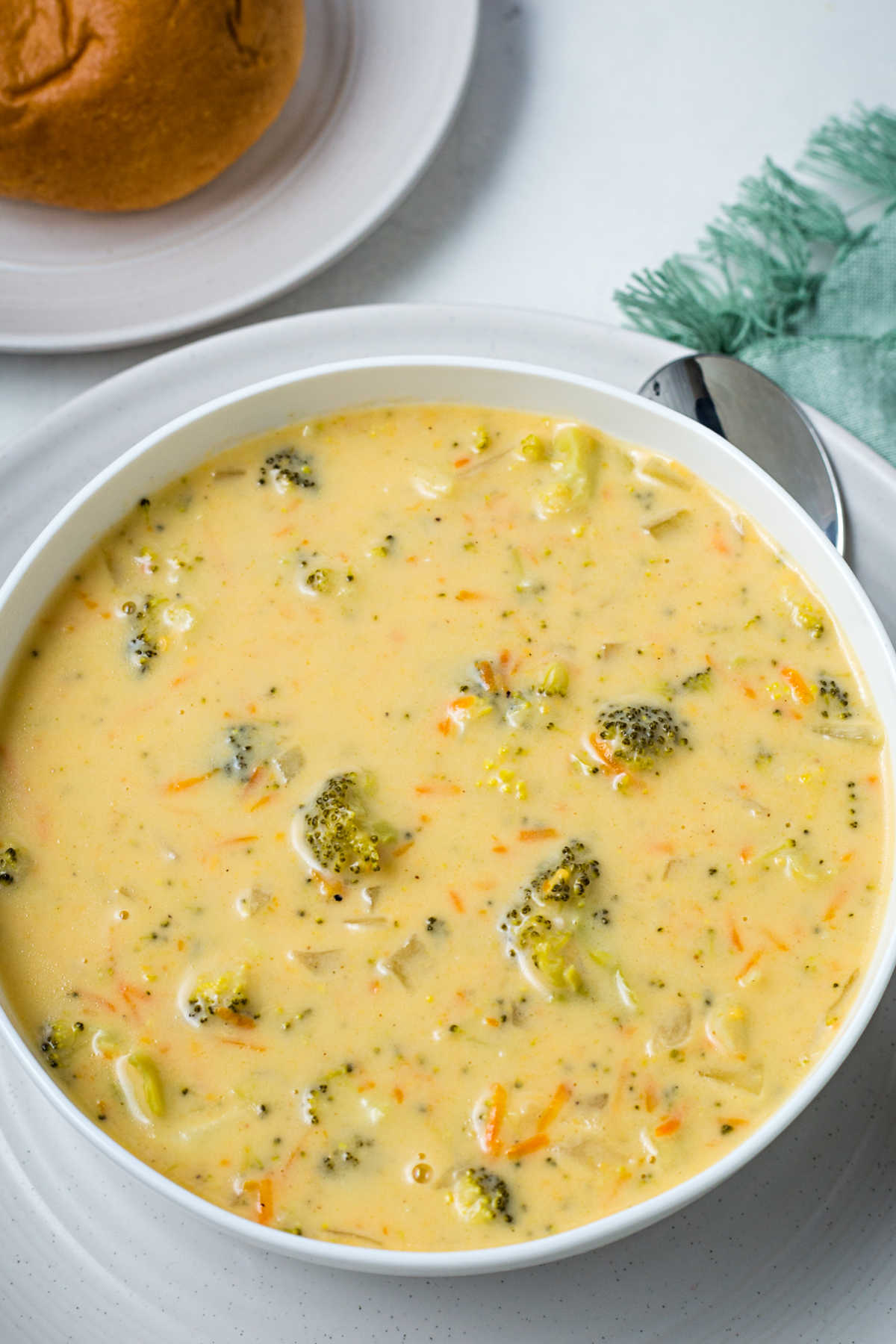 a bowl of broccoli cheddar soup on a table with a bread roll.