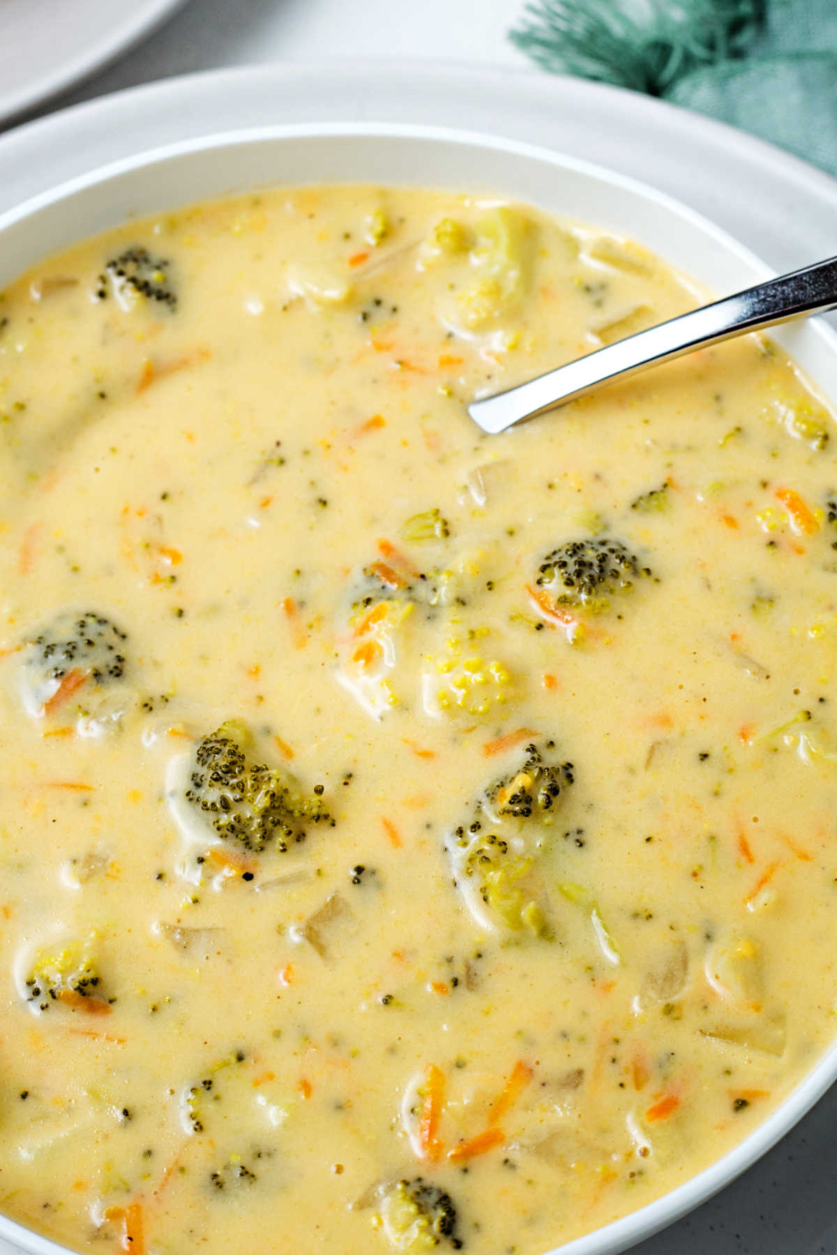 a close up shot of a bowl of crockpot broccoli cheddar soup with a spoon sticking out.