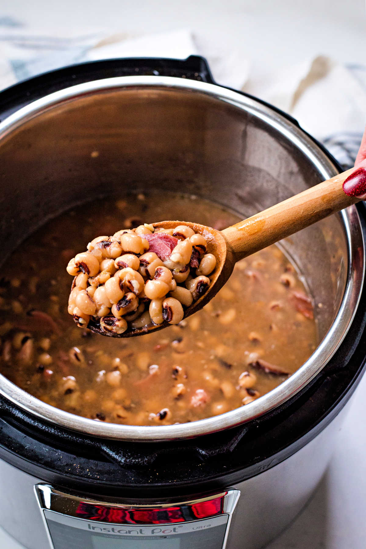 a wooden spoon lifting out black eyed peas from an instant pot.
