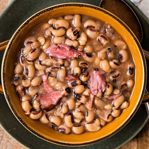 a bowl of black eyed peas with chunks of ham sitting on a plate.