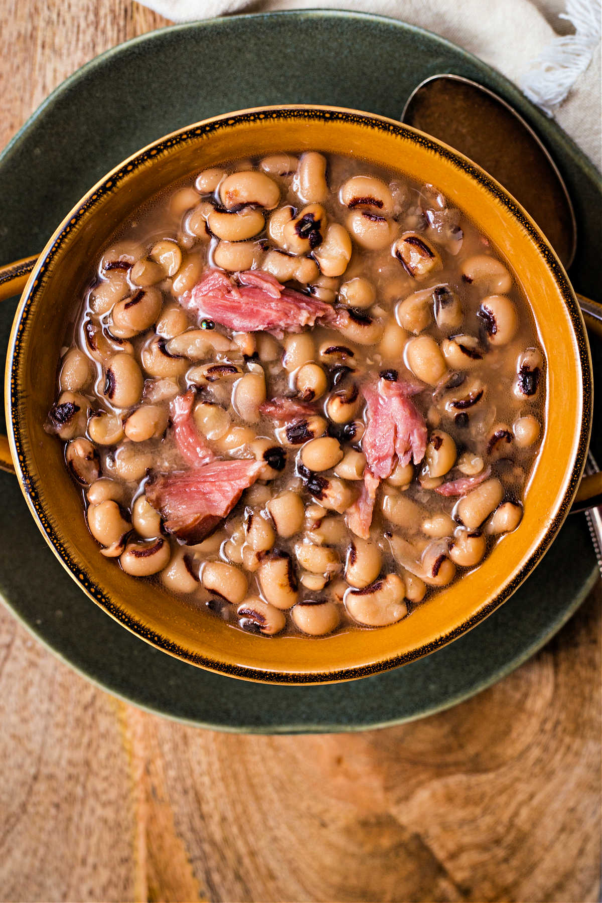 a bowl of black eyed peas with chunks of ham sitting on a plate.