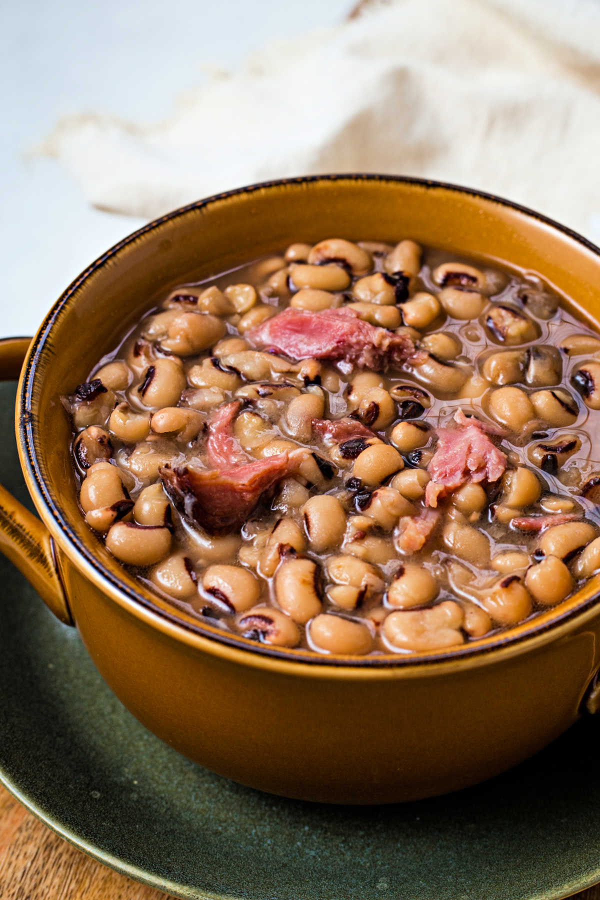 side view of a bowl of black eyed peas with chunks of ham sitting on a plate.