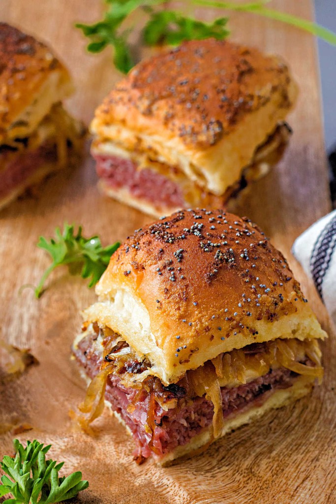 a roast beef slider on a wooden board with other sliders in the background.