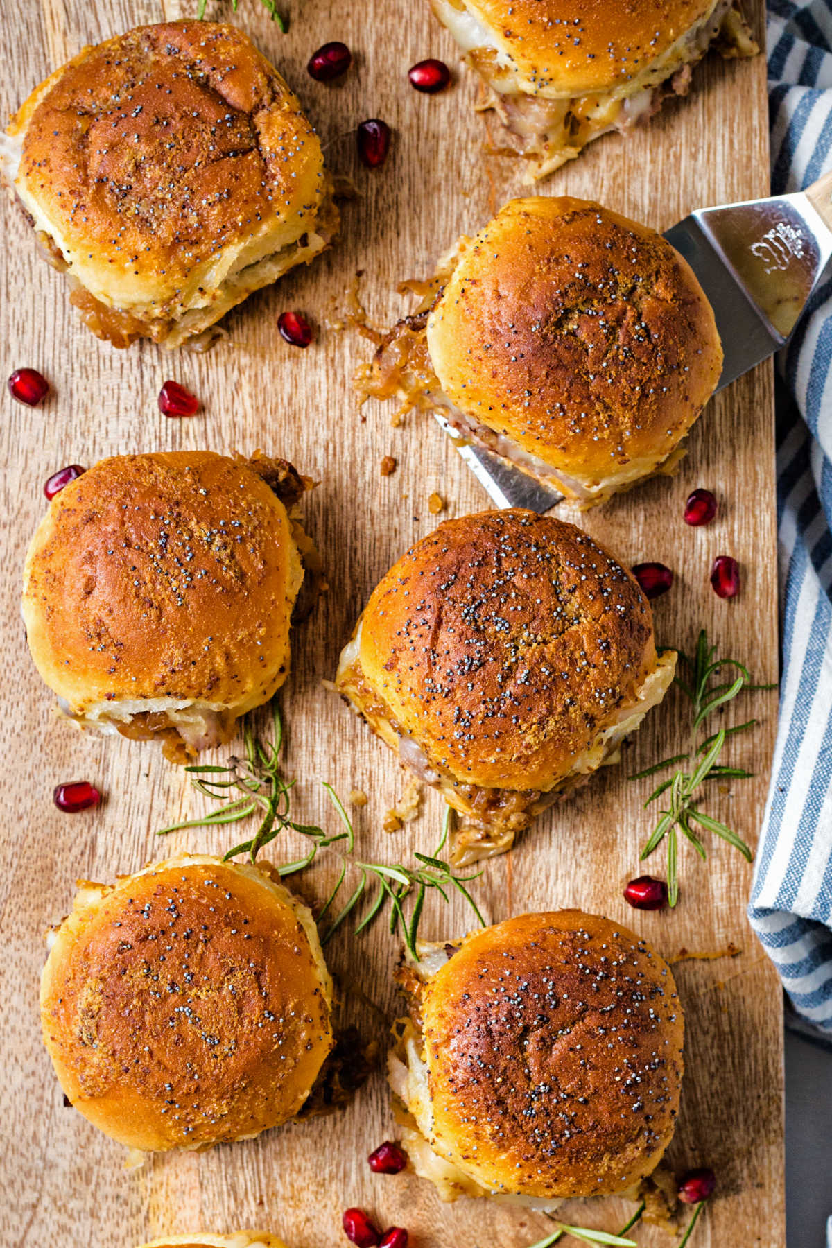 roast beef sliders on a wooden serving board with pomegranate seeds sprinkled aound.