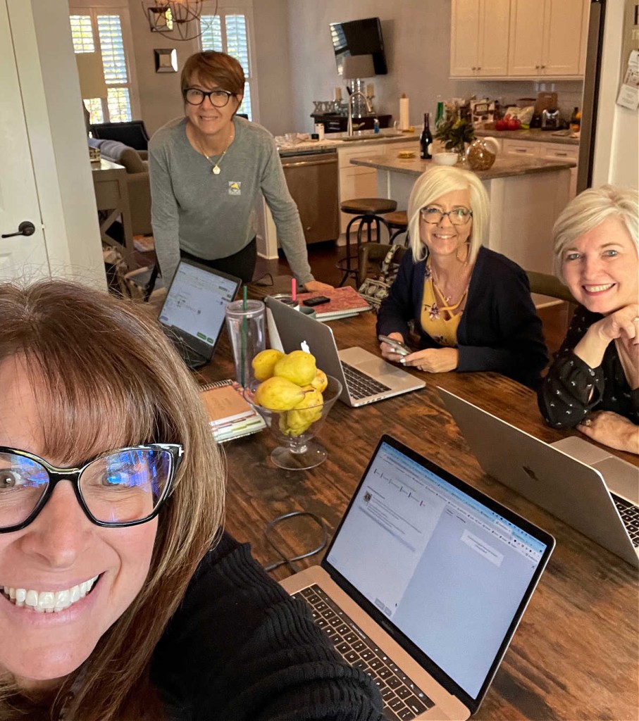 four women working on laptops sitting around a table.