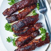 close up shot of barbecue sauce slathered country style ribs on a white platter garnished with parsley.