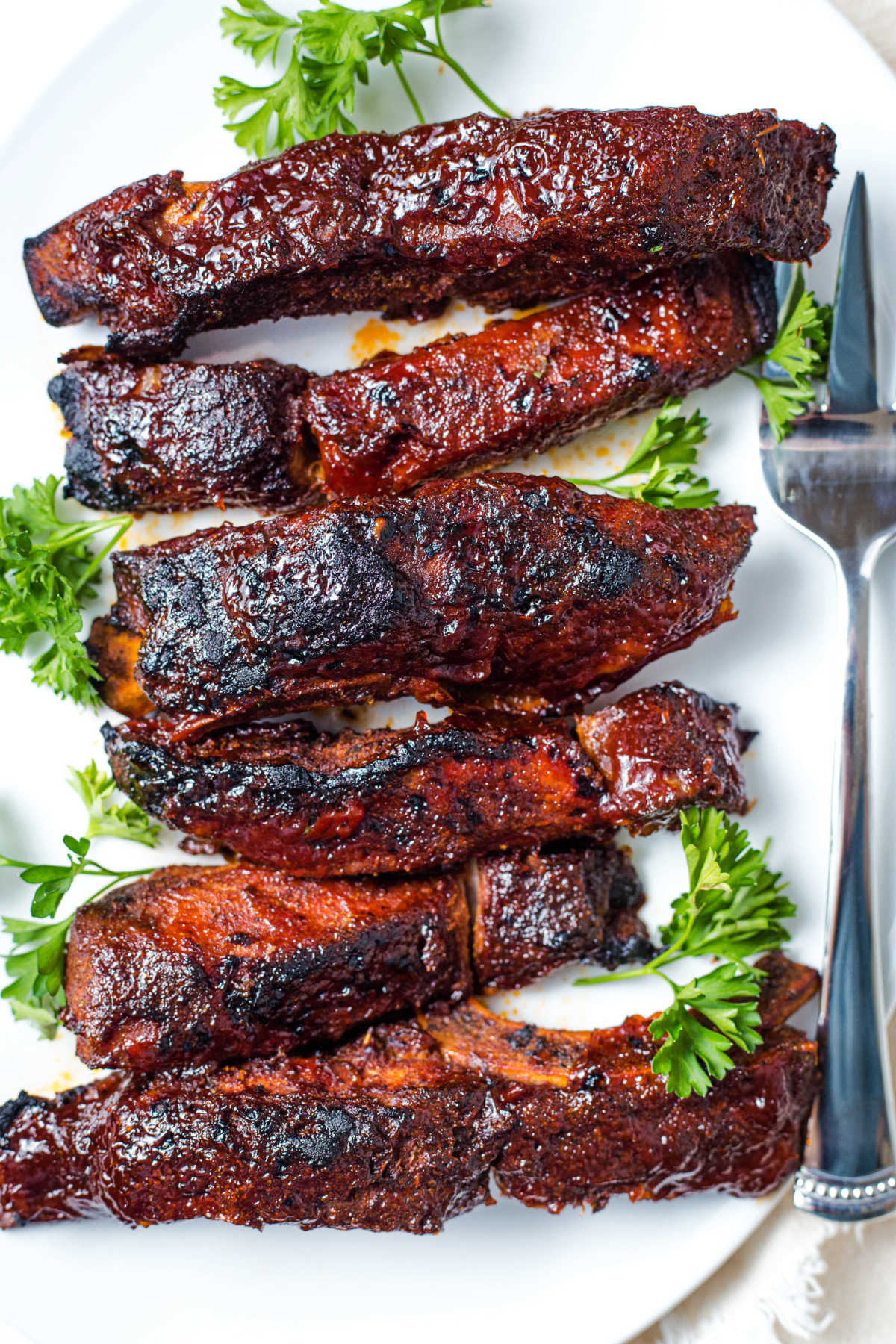 barbecue sauce slathered country style ribs on a white platter garnished with parsley.