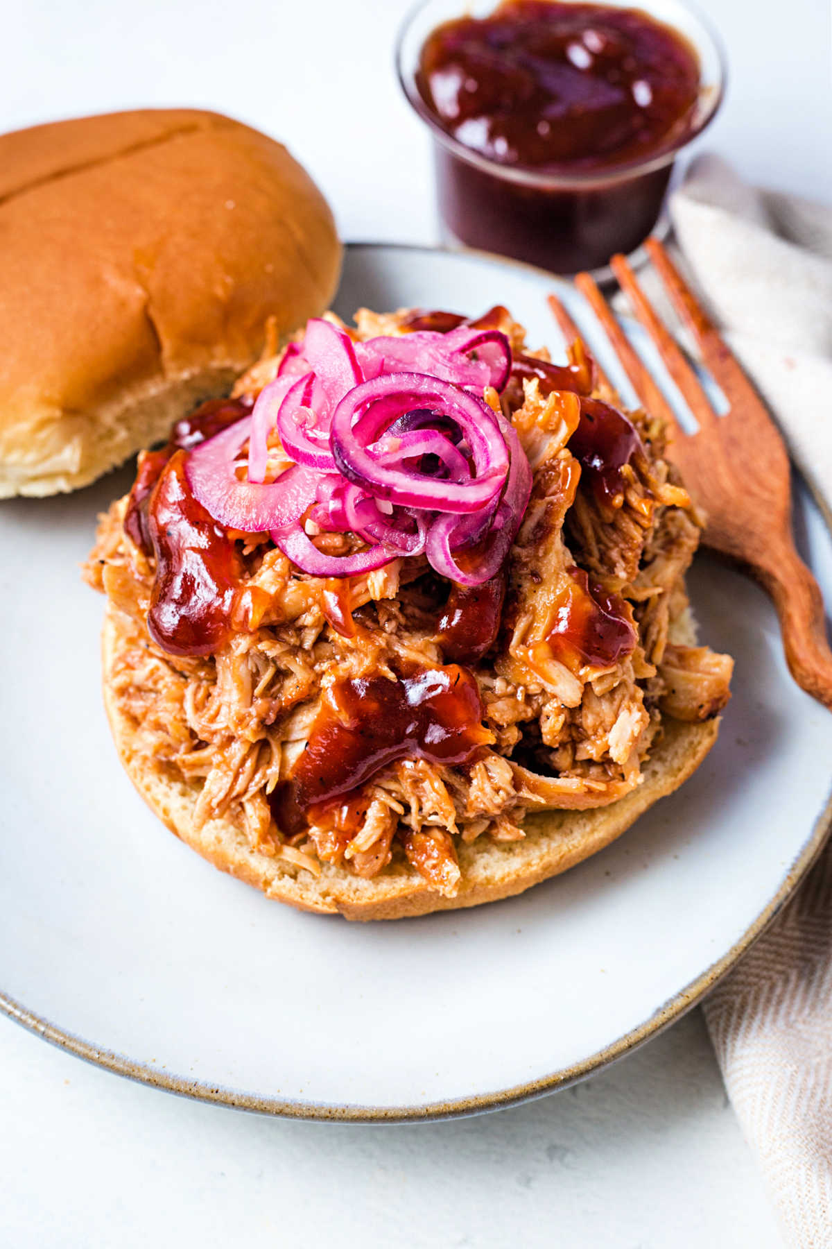 slow cooker pulled chicken on a bun with a side of barbecue sauce on a plate.