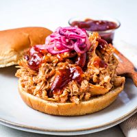 slow cooker pulled chicken piled high on a bun with pickled red onions as a garnish.