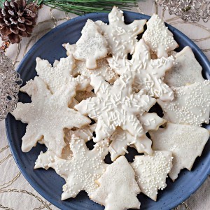 vanilla cookies in snowflake and tree shapes stacked on a blue plate.