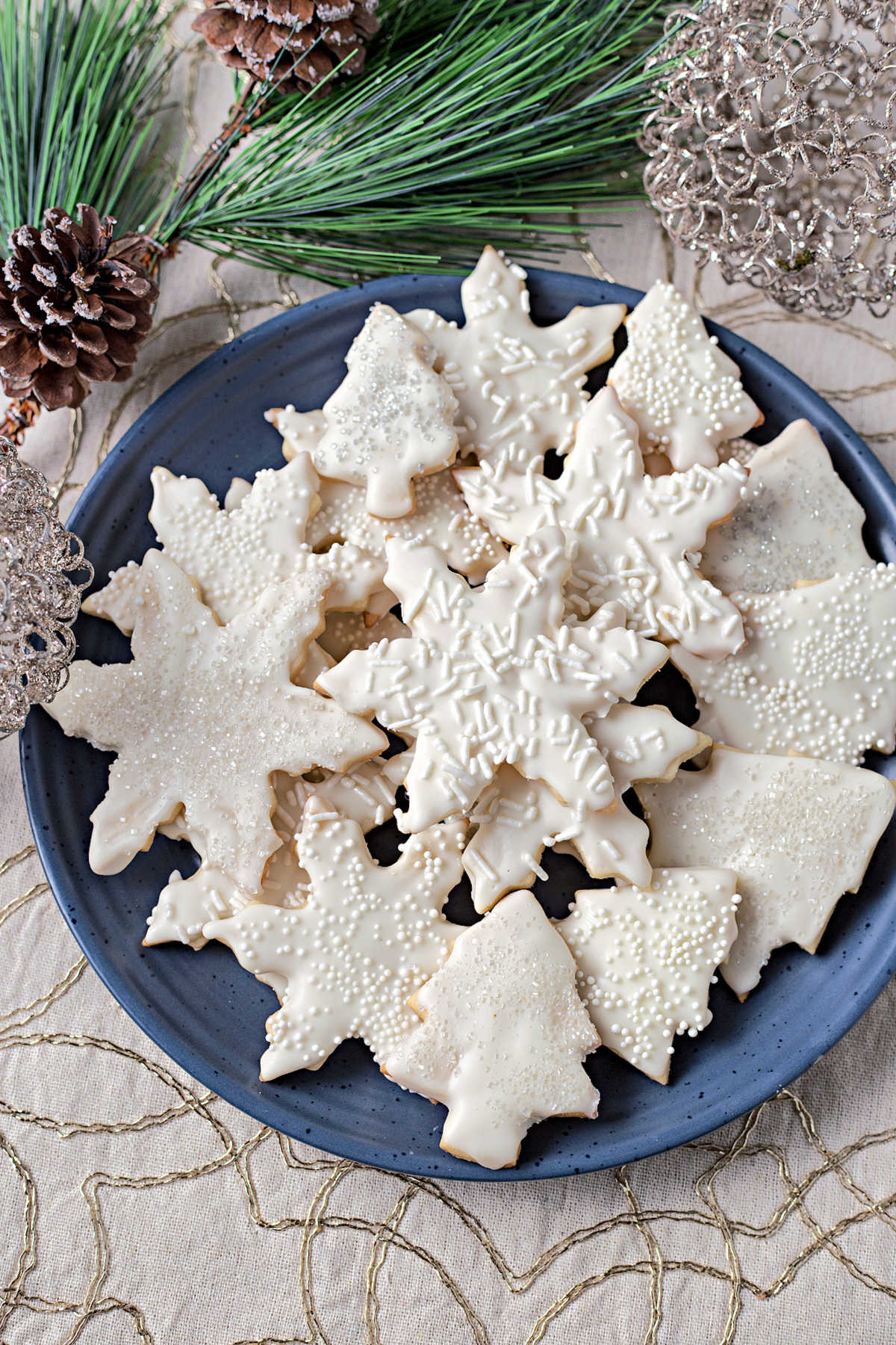 vanilla cookies in snowflake and tree shapes stacked on a blue plate.