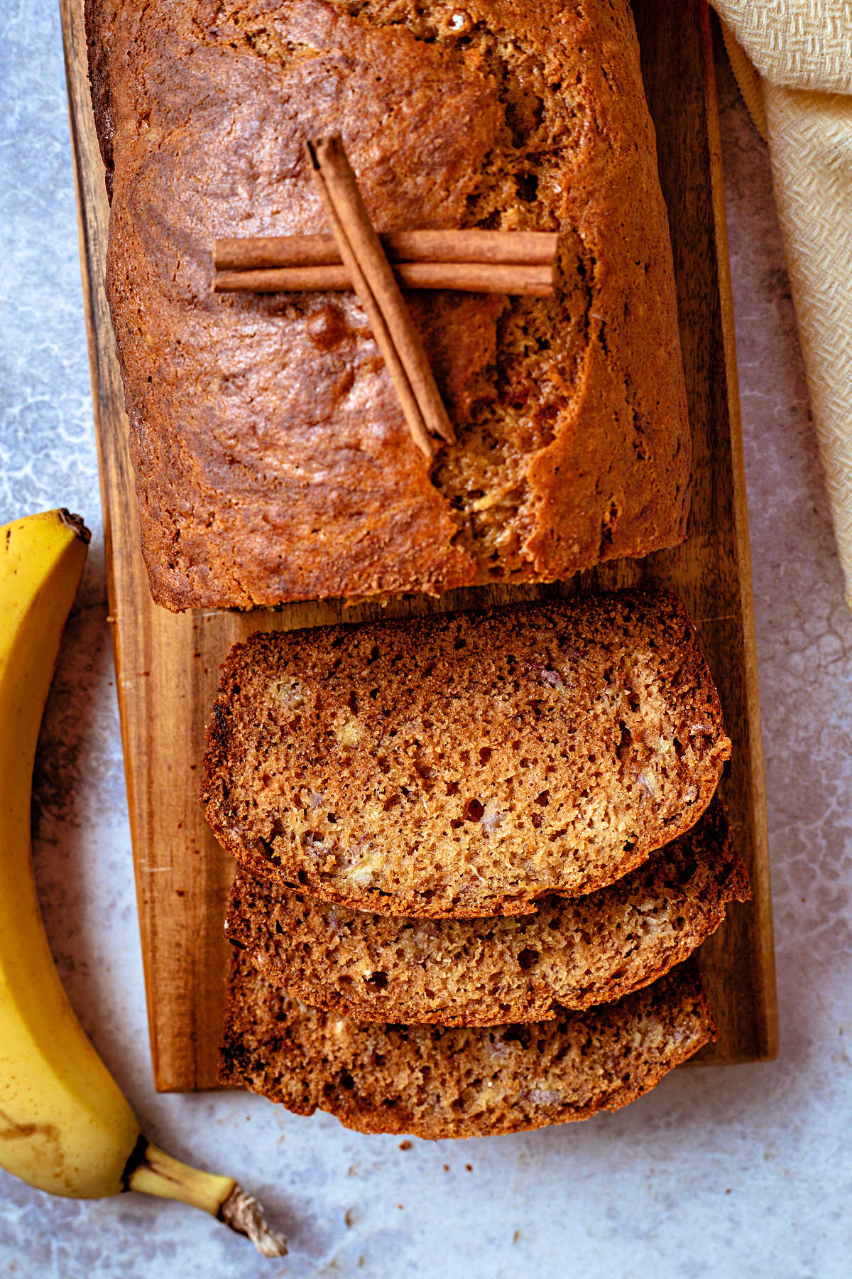 a partially sliced loaf of whole wheat banana bread on a wooden board with a banana to the side.
