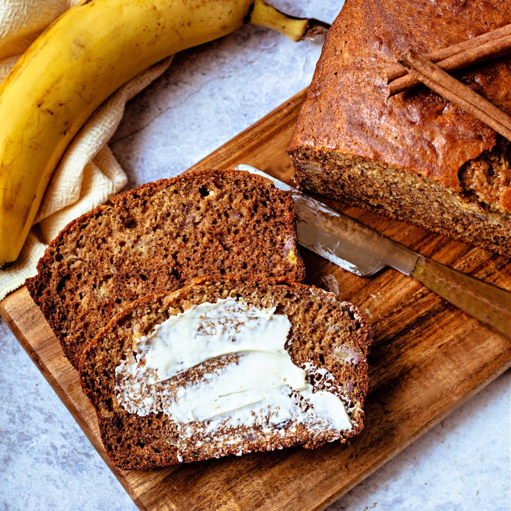 two slices of whole wheat banana bread with butter smeared on top on a wooden board.