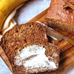 two slices of whole wheat banana brea on a cutting board smeared with butter.