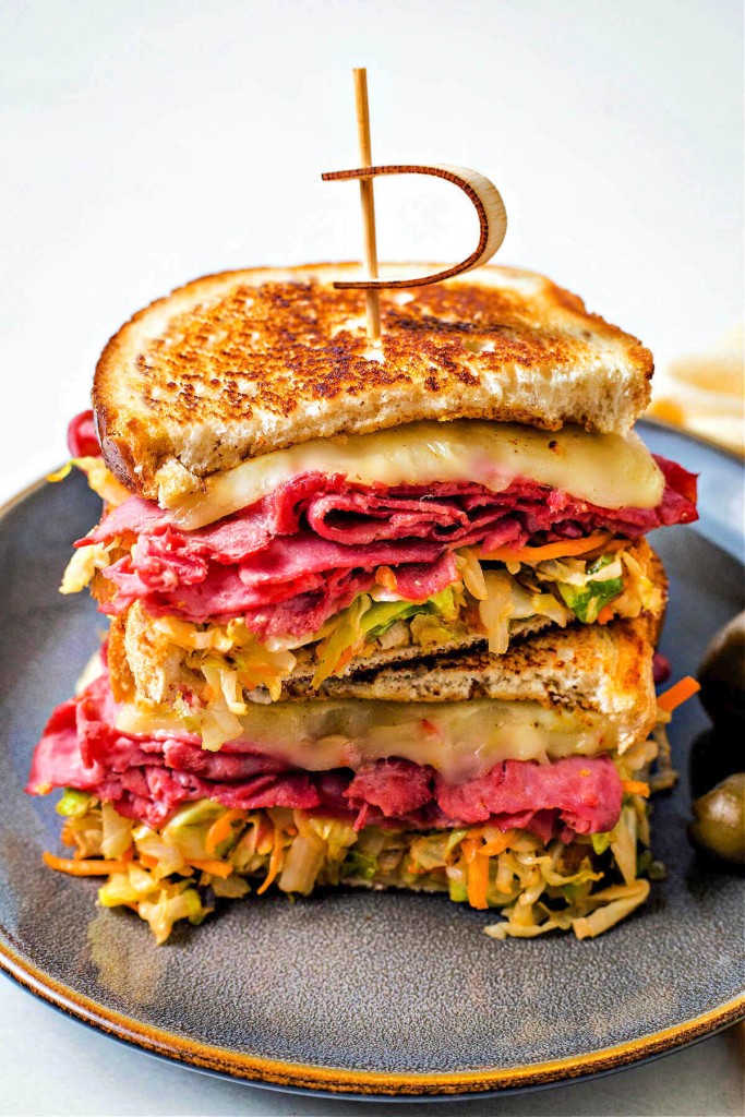 a corned beef reuben with coleslaw sandwich cut in half and stacked on a plate with a pick through the center.