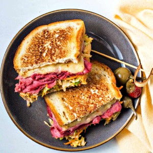 top down view of a corned beef reuben with coleslaw sandwich cut in half and stacked on a plate.