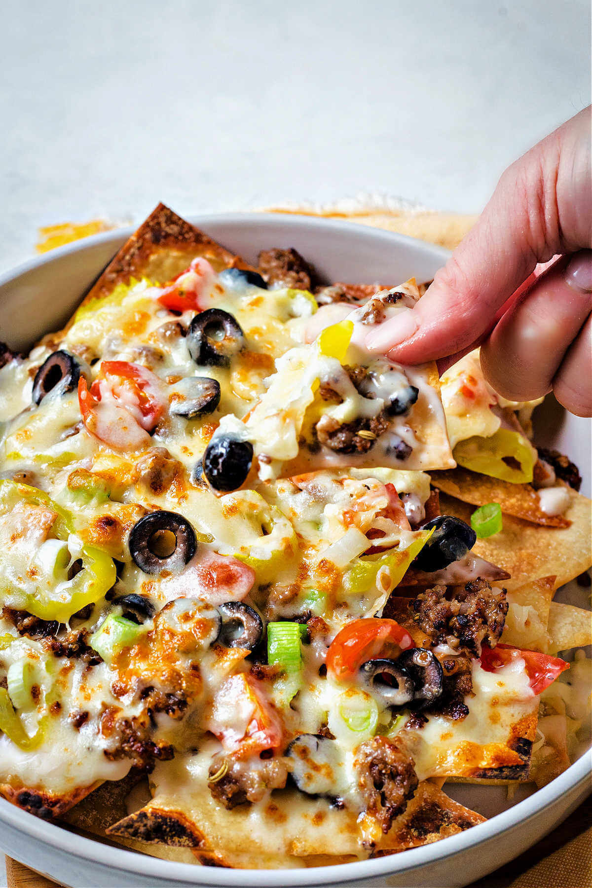 a hand picking up an Italian nacho from the pan.