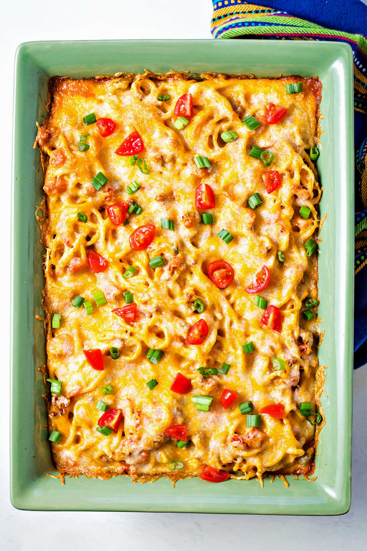 baked Mexican spaghetti in a casserole dish topped with sliced green onions and tomatoes.