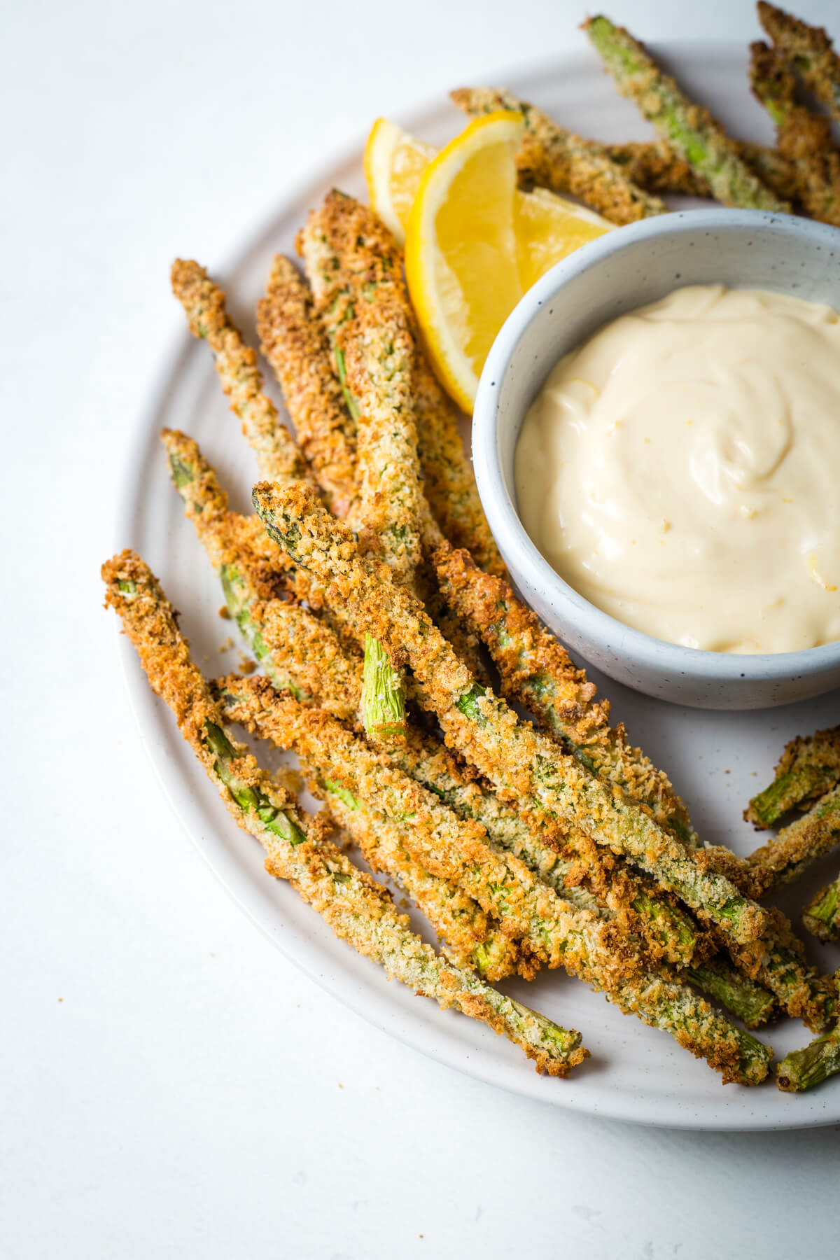 close up shot of air fryer asparagus veggie fries on a plate with a bowl of lemon garlic aioli for dipping.