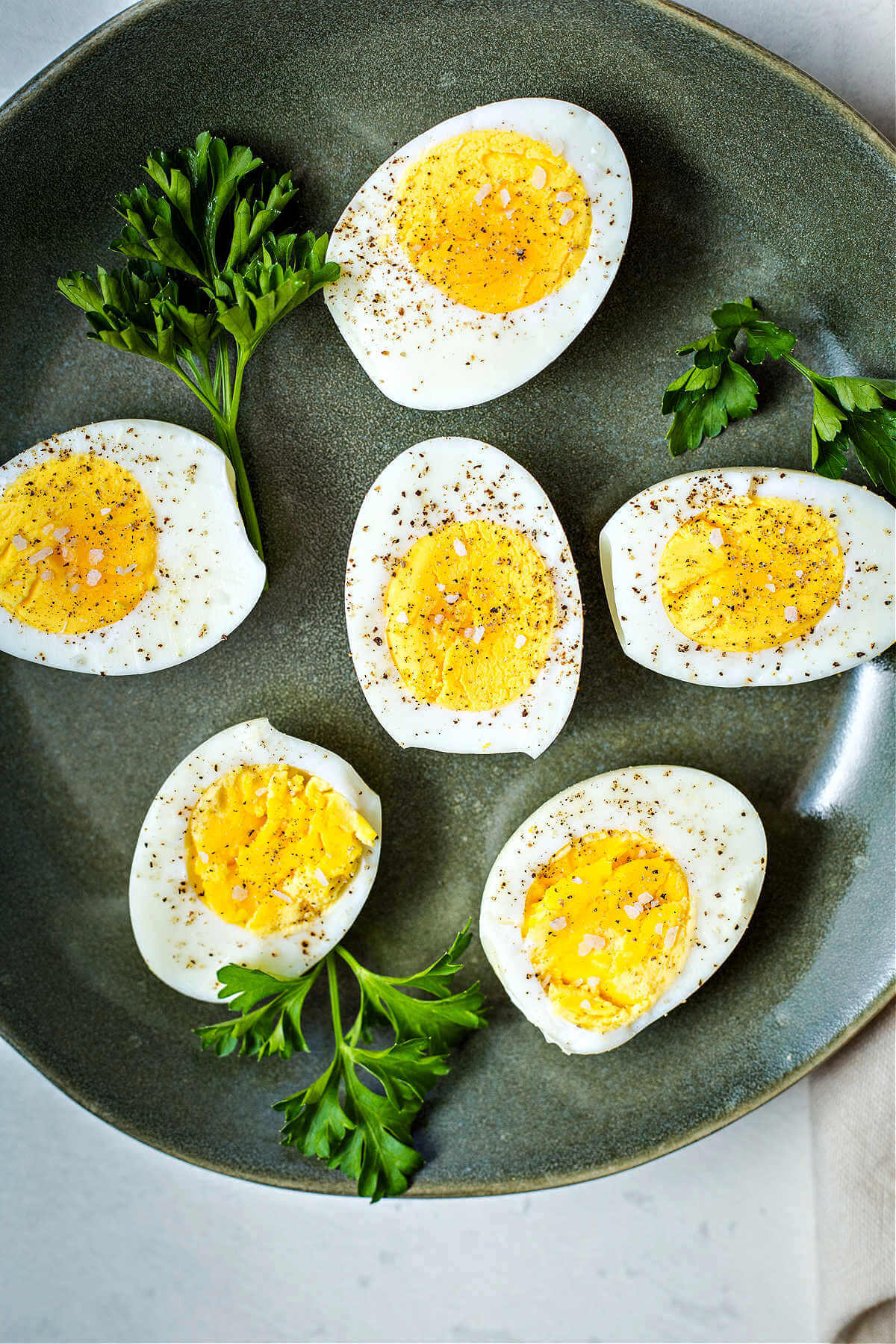 hard boiled eggs sliced in half and sprinkled with salt and pepper on a green plate with parsley garnish.